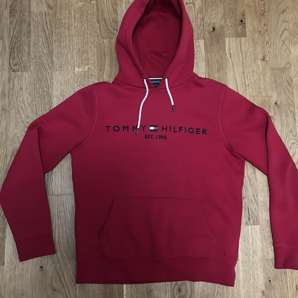 Säljer en snygg röd hoodie från Tommy Hilfiger. Den har en klassisk design med logotyp framtill och en praktisk magficka. Perfekt för en avslappnad stil. (STORLEK-M). Neuletakit & Villapaidat.