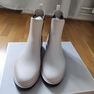 Tamaris Ankelstövlar, Beige, EUR 38 - Ett par stilrena ankelstövlar från Tamaris. Stövlarna har en bekväm design med resår i sidorna och en robust sula. Perfekt för både vardag och fest.  Tamaris Gummistövlar - ivory/black