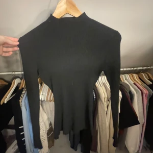 Svart ribbad tröja från H&M - Säljer en stilren svart ribbad tröja från H&M. Tröjan har en hög krage och långa ärmar. Den är tight i midjan. 