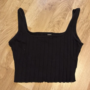 Svart ribbad linnetopp från Shein - Croppad svart ribbad linnetopp från Shein. Perfekt för en stilren look med sin croppade design och breda axelband. Passar utmärkt till både jeans och kjol.