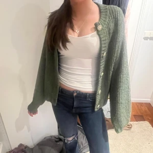 Grön stickad kofta med knappar - Säljer en mysig grön stickad kofta med knappar framtill. Koftan har en avslappnad passform och långa ärmar, perfekt för kyligare dagar. Den är enkel att matcha med olika outfits och ger en skön och stilren look.
