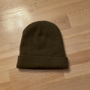Brun stickad mössa - Säljer en enkel och stilren brun stickad mössa. Perfekt för att hålla värmen under kyliga dagar. Mössan har en klassisk design med uppvikt kant. Den är ej använd och och är helt ny😁