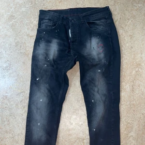 Svarta jeans från Dsquared2 - Snygga svarta jeans från Dsquared2 med en cool sliten look och unika detaljer. Byxorna har en diskret logga på fickan och en färgglad patch på baksidan. Perfekta för dig som vill ha en edgy stil.