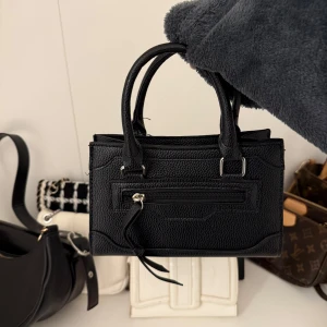 Svart liten väska  - Säljer en söt liten svart väska, passar perfekt till en utgång eller vardag när man vill ha med sig det viktigaste som till exempel, plånbok, läppglans, nycklarna osv