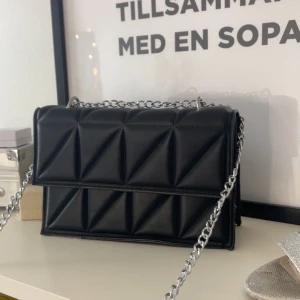 Svart axelväska - Snygg svart axelväska och en stilren kedja som axelrem. Den har använts få gånger och är i väldigt bra skick💞💞Väskan har en praktisk magnetknäppning och är perfekt för att bära dina nödvändigheter med stil. Den har en modern design som passar till många olika outfits.