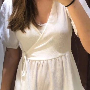 Vit omlottklänning från Gina Tricot - Vit omlottklänning från Gina Tricot. Klänningen har en v-ringad design och trekvartsärmar med en knytning i midjan för en smickrande passform. Perfekt för sommarens alla tillfällen!😍