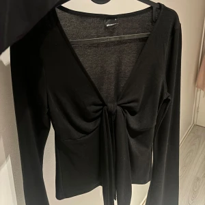 Svart långärmad topp från Gina Tricot - Snygg svart långärmad topp från Gina Tricot med knytning framtill. Perfekt för en stilren look. Toppen har en v-ringad design som ger en elegant touch. Använd en gång