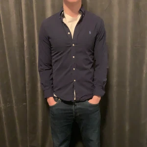 Mörkblå skjorta från Ralph Lauren - Snygg mörkblå skjorta från Ralph Lauren i slim fit. Skjortan har långa ärmar och knappar framtill. Perfekt för en stilren look.