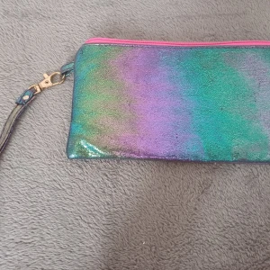 Glittrig flerfärgad kuvertväska - Säljer en glittrig kuvertväska i flerfärgat material med en rosa dragkedja. Väskan har en avtagbar rem med en guldfärgad hake. Insidan är fodrad i rosa tyg. Perfekt för att ge en färgglad touch till din outfit!