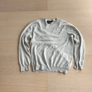 Grå tröja från Ralph Lauren - Säljer en stilren grå tröja från Ralph Lauren i Pima bomull. Tröjan har en slim fit passform och långa ärmar. Den är perfekt för en klassisk och avslappnad look. Ralph Laurens ikoniska logga är broderad på bröstet.