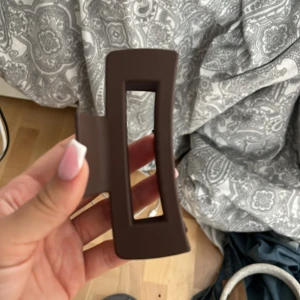 Brun hårklämma - Säljer en stilren brun hårklämma i plast med rektangulär form. Perfekt för att hålla håret på plats med ett enkelt och elegant grepp. Passar både för vardag och speciella tillfällen.