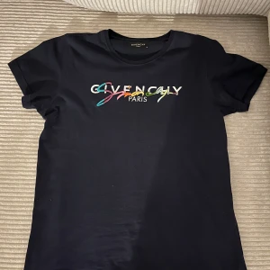 Svart t-shirt från Givenchy - Säljer en svart t-shirt från Givenchy med färgglatt broderat logotyp på bröstet. T-shirten har en klassisk rund hals och korta ärmar. Perfekt för en stilren look med en touch av färg.perfekt för sommar. Det går att pruta priset vid frågor skriv bara 💬!