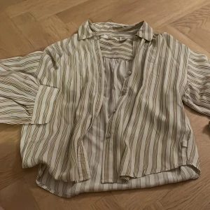 Randig skjorta från Levi's - Säljer en snygg randig skjorta från Levi's i storlek XS. Skjortan har en klassisk krage och knappar framtill. Den är vit med tunna svarta och beige ränder, vilket ger en stilren look. Perfekt för dig som gillar en tidlös stil!