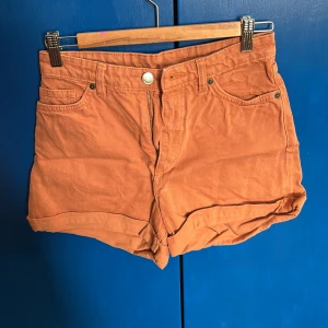 Orange shorts från Monki - Högmidjade snygga orange shorts från Monki med klassisk femficksdesign och knappgylf. Även växt ur dessa men tycker dem är ur söta, även lite vintage look över dem😆