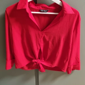 Röd knytblus från Select - Snygg röd blus från Select med knytning framtill. Blusen har trekvartsärmar och en klassisk krage. Perfekt för en färgglad look!