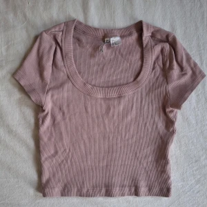 Ribbad rosa topp från H&M Divided - Säljer en söt ribbad och kroppad rosa topp från H&M Divided. Den har en rundad halsringning och korta ärmar, perfekt för en avslappnad stil. Toppen är i en mjuk och bekväm bomullsmix. 