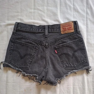 Svarta jeansshorts från Levi's - Snygga svarta jeansshorts från Levi's med fransiga kanter och klassiska femficksdesign. Perfekta för en avslappnad stil. De har en knappgylf och är tillverkade i slitstarkt denim.