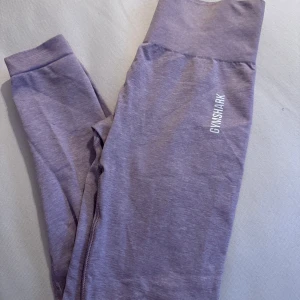 Lila/rosa leggings från Gymshark - Snygga lila leggings från Gymshark med hög midja och en tight passform. Perfekta för träning med en bekväm och stretchig design. Gymshark-loggan är tryckt på sidan av benet.
