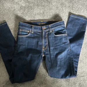 Mörkblå jeans från Nudie Jeans - Snygga mörkblå jeans från Nudie Jeans med klassisk femficksdesign och kontrastsömmar. Jeansen har en normal passform och är tillverkade i slitstarkt denim. Perfekta för en stilren look.