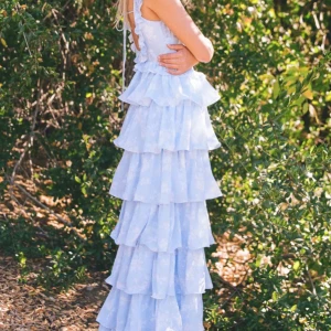 Ljusblå långklänning med volanger - Charmig ljusblå långklänning med volanger och blommigt mönster. Klänningen har ärmlös design och en öppen rygg med knytband. Perfekt för somriga tillfällen. Nypris : 2699 :-