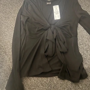 Svart långärmad topp med knyt - Svart topp med knytning från Gina. Aldrig använd 