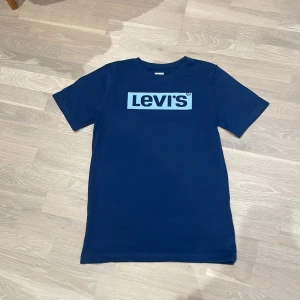 Mörkblå t-shirt från Levi's - Säljer en snygg mörkblå t-shirt från Levi's med deras ikoniska logga i vitt på bröstet. Perfekt för en avslappnad stil. Tillverkad i mjukt material för extra komfort. Storlek XS/S