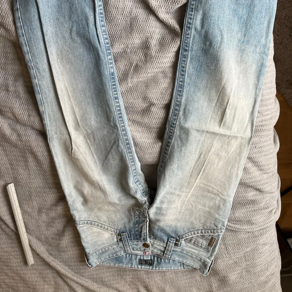 Snygga ljusblå baggy lågmidjade jeans med en klassisk femficksdesign. De har en sliten look med ljusare partier vit text bak . Perfekta för en 2000 tal cool look. Farkut & Housut.