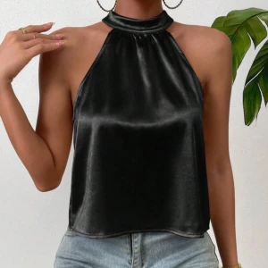 Svart halterneck topp med öppen rygg - Snygg svart halterneck topp i satin med en elegant öppen rygg och glittrande detaljer. Perfekt för en kväll ute eller en speciell tillställning. Toppen har en lös passform och ger en lyxig känsla.
