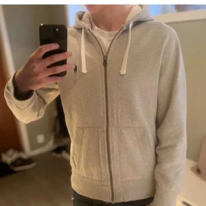 Grå hoodie från Polo Ralph Lauren - Säljer en stilren grå hoodie från Polo Ralph Lauren med dragkedja och huva. Tröjan har långa ärmar och en liten broderad logga på bröstet. Perfekt för en avslappnad stil. Bra skick. Hör av dig vid funderingar //Tom