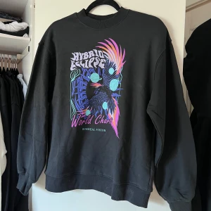 Svart/mörkgrå sweatshirt med färgglatt tryck - Säljer en svart sweatshirt från H&M Divided med ett coolt och färgglatt tryck. Tröjan har långa ärmar och ribbade muddar vid ärmslut och nederkant. Perfekt för en avslappnad stil! Oanvänd! Önskar du veta exakta mått? Tveka inte att höra av dig!