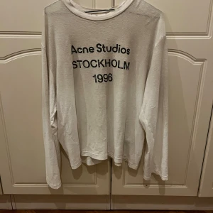 Vit långärmad tröja från Acne Studios - Säljer en stilren vit långärmad tröja från Acne Studios med tryck 'STOCKHOLM 1996' på framsidan. Perfekt för en minimalistisk look. Tröjan har en rund halsringning och är tillverkad i ett mjukt material. Skräddarsydd så att längden är ca 60cm. Passar mig som är 175