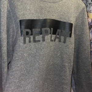 Grå sweatshirt från Replay - Snygg grå sweatshirt från Replay med ett stort svart tryck på bröstet. Tröjan har långa ärmar och en klassisk rund halsringning. Perfekt för en avslappnad stil.
