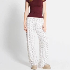 Vita byxor med hjärtmönster - Snygga vita byxor med små röda hjärtan. De har en loose passform och är perfekta för en avslappnad stil. Byxorna är tillverkade i ett mjukt och bekvämt material.