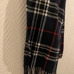 Rutig halsduk i mörka färger - Snygg rutig halsduk med mörkblå, vita och röda rutor. Perfekt för att hålla sig varm under kyliga dagar. Den har fransar i ändarna som ger en extra touch av stil. 110kr✅