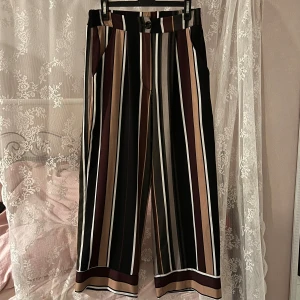 Randiga byxor i olika färger - Snygga randiga byxor med breda ben i svart, beige, brun och vit. Byxorna har en knapp och dragkedja framtill samt fickor på sidorna. Dom ser korta ut på mig men det är bara för att jag är 168! :’) Köpte dom på sellpy för ett par år sen men har knappast användt dom så det är nu dags att dom får ett nytt hem 💕Rivmärkena på sista bilden är förmodligen från min katt, men det är inget som egentligen syns jättebra eller något man tänker på!