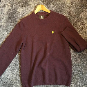 Vinröd tröja från Lyle & Scott - Vinröd tröja från Lyle & Scott i ett lite ruffigare material som är perfekt till kyliga vårdagar och sommakvällar. Passar både till jeans och chinos för en avslappnad look. Kan också kombineras med skjorta för en mer formel stil. 
