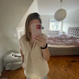 Beige fleeceväst från BikBok - Säljer en mysig beige fleeceväst från BikBok i storlek L men passar mig som har storlek S. Västen har en dragkedja framtill och är perfekt för att hålla värmen. Den har en enkel och stilren design som passar till många olika outfits.