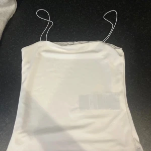 Vit satinlinne från Amisu - Säljer ett stilrent vitt satinlinne från Amisu med tunna axelband. Perfekt för en elegant look. Passar bra till både jeans och kjol. 🌟