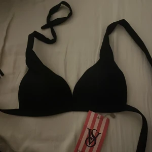 Svart bikiniöverdel från Victoria's Secret - Snygg svart bikiniöverdel från Victoria's Secret med knytband i nacken. Den har en enkel och stilren design med vadderade kupor för extra komfort. Perfekt för en dag på stranden eller vid poolen.