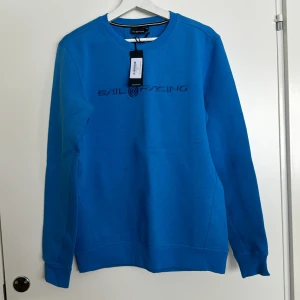 Blå tröja från Sail Racing - Säljer en snygg blå tröja från Sail Racing med text på bröstet. Tröjan har långa ärmar och en rund halsringning. Perfekt för en avslappnad stil. Storlek M. Helt ny. Inga defekter.