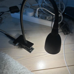 Svart klämspotlight med flexibel arm - Praktisk svart klämspotlight med en flexibel arm som gör det enkelt att rikta ljuset. Lampan har en klämma för enkel fastsättning på bord eller hyllor. Perfekt för läsning eller arbete vid skrivbordet.