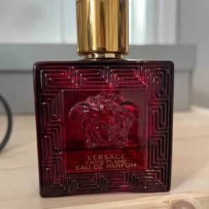 Versace Eros Flame Eau de Parfum - Säljer en elegant Versace Eros Flame Eau de Parfum i en djup röd flaska med guldlock. Flaskan har ett detaljerat mönster och den ikoniska Medusa-loggan. Perfekt för den som vill ha en doft med både intensitet och stil. Inte så mycket kvar i den men jag skulle gissa på 10ml.