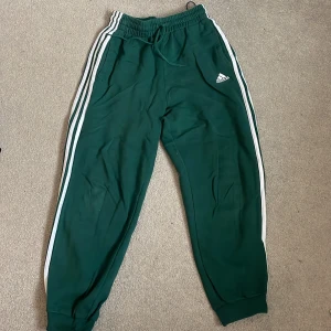 Gröna mjukisbyxor från Adidas - Snygga gröna mjukisbyxor från Adidas. Byxorna har en elastisk midja med snörning och muddar vid bensluten. 