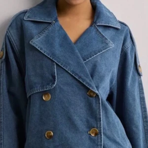 Blå jeansjacka med knappar - Säljer en snygg blå jeansjacka med dubbelknäppning och stora kragar. Jackan har en cool oversized passform och knappar i trälook. Perfekt för en avslappnad stil.