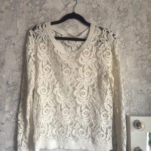 Vit spetsblus från Samsøe Samsøe - Säljer en elegant vit spetsblus från Samsøe Samsøe med vackert blommönster. Blusen har långa ärmar och en ribbad kant vid halsringningen. Perfekt för att ge en fin touch till din outfit. Super fin fest tröja. 