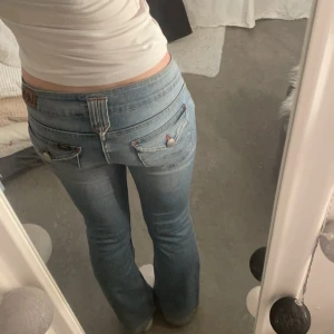 Blå jeans från Lee - Snygga blå bootcut jeans från Lee. Byxorna har en lågmidjad passform och dekorativa bakfickor med knappar. Perfekta för en avslappnad look.