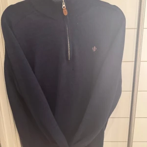 Mörkblå tröja med dragkedja från Morris - Säljer en stilren mörkblå tröja från Morris med en praktisk dragkedja framtill. Tröjan har en liten broderad logotyp på bröstet och är perfekt för kyligare dagar. Passar bra till både jeans och chinos. Litet hål men går att sy, därav priset:)