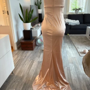 Champagnefärgad långklänning - Elegant champagnefärgad långklänning i satin med omlott-design och v-ringning. Klänningen har en smickrande passform och en slits som ger extra rörelsefrihet. Perfekt för speciella tillfällen.