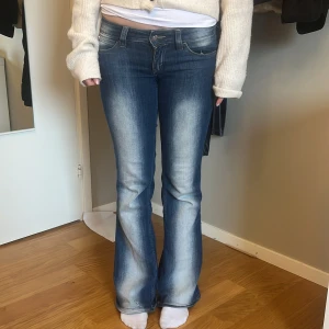 Blå bootcut jeans - Snygga blå bootcut jeans med en klassisk femficksdesign. Jeansen har en lätt tvättad look och är perfekta för en avslappnad stil. De är lågmidjade och har en dragkedja framtill.