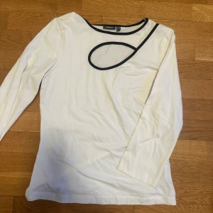 Vit långärmad topp från Gerry Weber - Snygg vit långärmad topp från Gerry Weber med unik svart kantdetalj runt halsen. Perfekt för en stilren look. Passar bra till både jeans och kjol. 🖤
